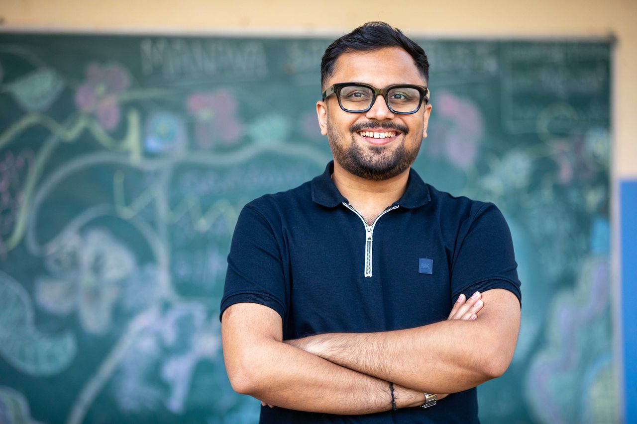 Smiling educator standing confidently in front of a chalkboard, exuding positivity and professionalism.