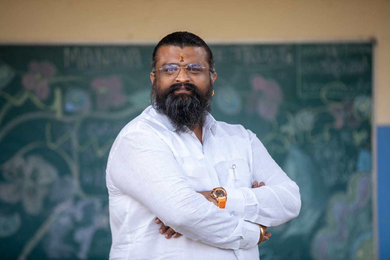 A confident man with folded arms stands in front of a chalk-drawn blackboard.