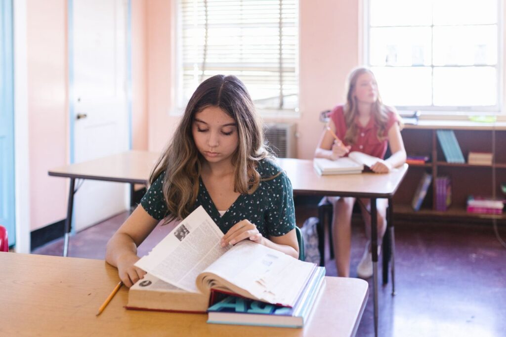 Two students engaging with books in a classroom setting, focused on learning and study.