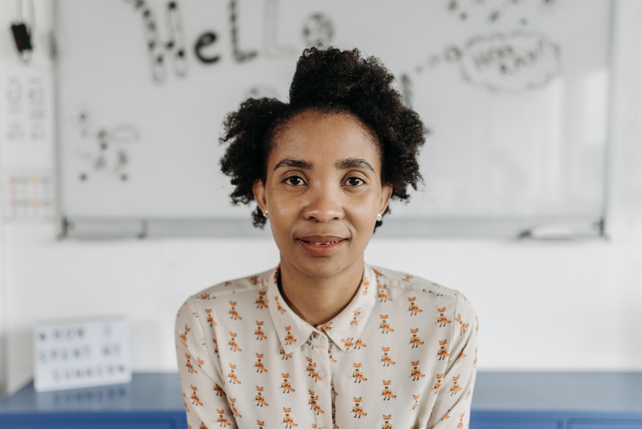 A confident woman with afro hair poses in a classroom, fostering an educational theme.